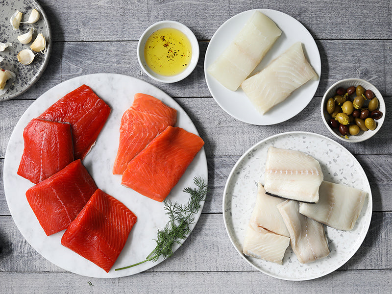 Wild Alaska Sockeye and Coho Salmon Portions, Wild Alaska Pacific Halibut Portions, and Wild Alaska Black Cod Portions on Plates on Wood Table