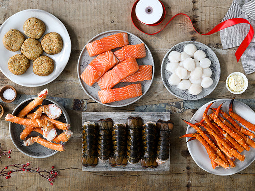 Atlantic Salmon Portions, Sea Scallops, King Crab Legs, Cold Water Lobster Tails, and Crab Cakes on Wood Table with Gift Ribbon Unraveling