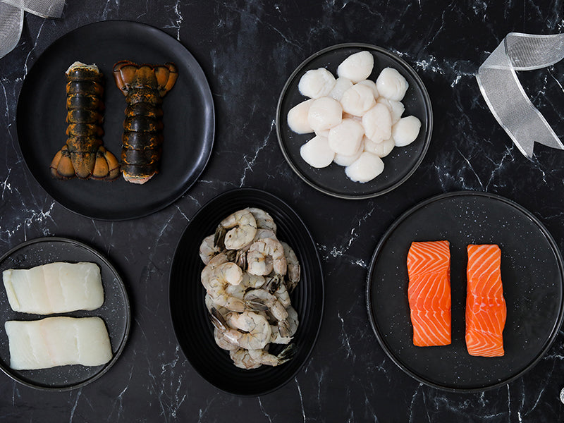 New Year's Eve Seafood Bundle with Scallops, Shrimp, Atlantic Halibut, Atlantic Salmon, and Lobster Tails on Dark Marble Surface with Gift Ribbons