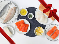 Atlantic Cod, Atlantic Salmon, Rainbow Trout, Arctic Char, Chilean Sea Bass, and Branzino on Plates with Lemon Wedges and Herbs with Gift Ribbon