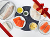 Atlantic Cod, Atlantic Salmon, Rainbow Trout, Arctic Char, Chilean Sea Bass, and Branzino on Plates with Lemon Wedges and Herbs with Gift Ribbon
