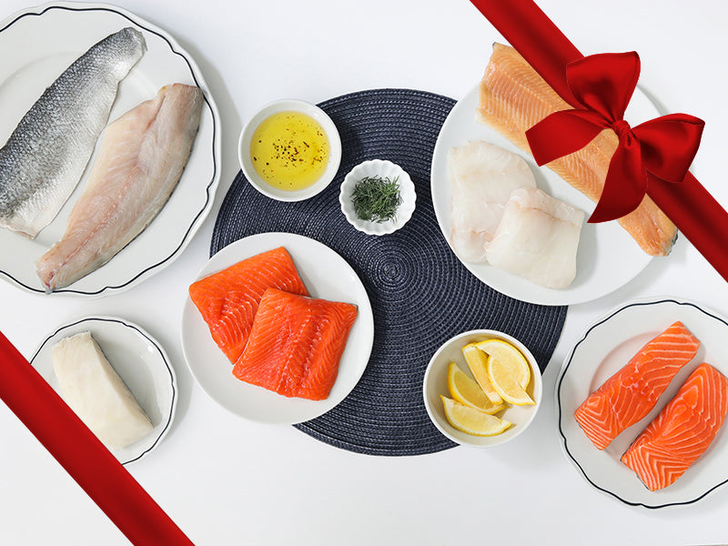 Atlantic Cod, Atlantic Salmon, Rainbow Trout, Arctic Char, Chilean Sea Bass, and Branzino on Plates with Lemon Wedges and Herbs with Gift Ribbon