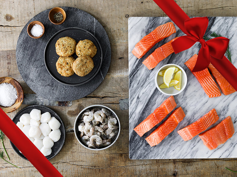 King Salmon Portions, Scallops, Shrimp, and Crab Cakes on Plates with Seasoning and Lemon Wedges with Gift Ribbon