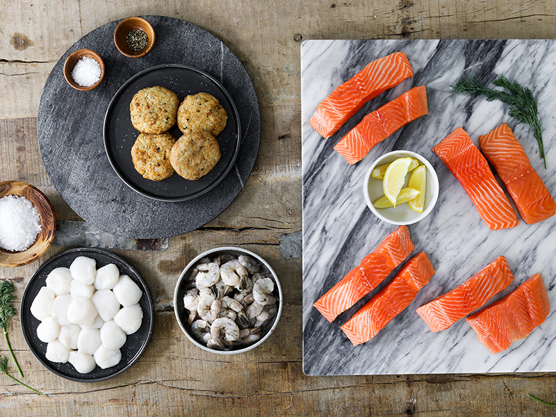 King Salmon Portions, Shrimp, Scallops and Crab Cakes on Plates and Trays with on Wooden Table