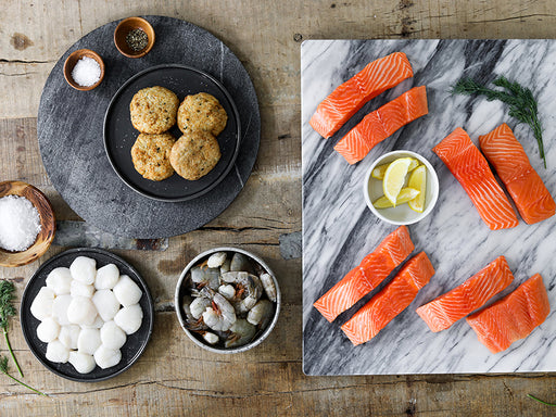 King Salmon Portions, Shrimp, Scallops and Crab Cakes on Plates and Trays with on Wooden Table