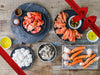 Golden King Crab Legs, Smoked Salmon, Shrimp, Scallops, and Cooked Lobster Meat on Plates on Wood Table with Gift Ribbon