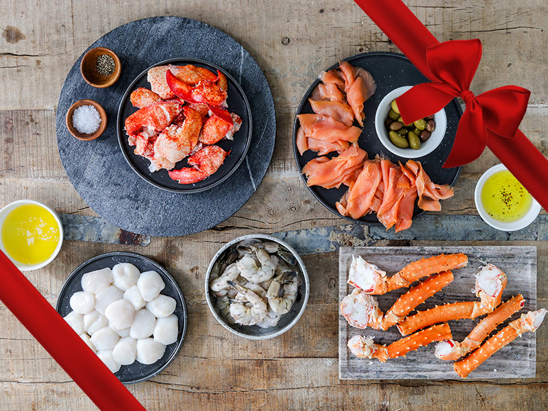 Golden King Crab Legs, Smoked Salmon, Shrimp, Scallops, and Cooked Lobster Meat on Plates on Wood Table with Gift Ribbon