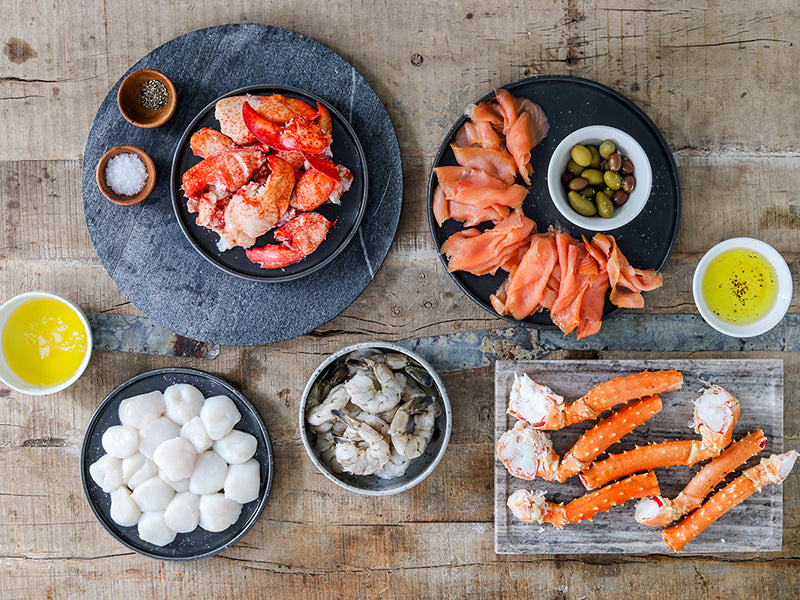 Smoked Salmon, Shrimp, Cooked Lobster Meat, Scallops, and Crab Legs on Plates on Wooden Table