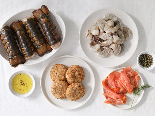 Assorted Seafood on Dishes including Lobster Tails, Shrimp, Smoked Salmon, and Crab Cakes on a White Surface