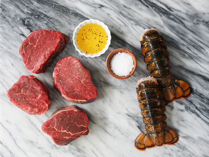 Four Filet Mignon Steaks and Two Lobster Tails on Marble Surface with Olive Oil and Salt