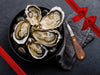 Fulton Fish Market Oyster Knife Next to Bowl of Shucked Oysters on the Half Shell with Gift Bow Graphic on Top Right