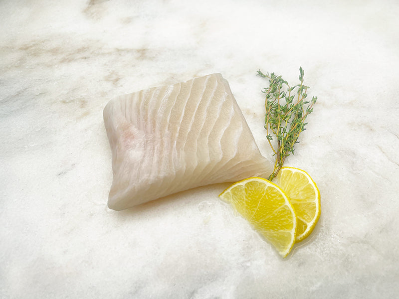 Atlantic Halibut Portion on Marble Surface with Lemon Wedges and Herbs