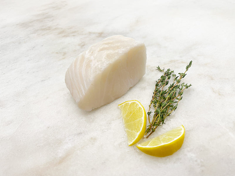 Chilean Sea Bass Portion on Marble Surface with Lemon Wedges and Herbs