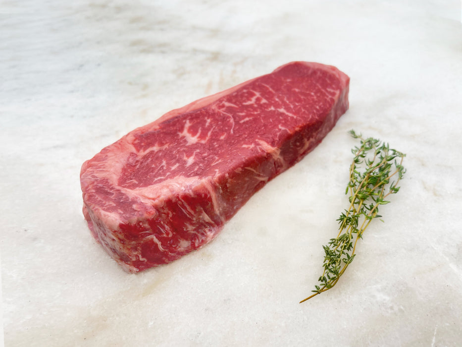 Pat LaFrieda Prime Boneless New York Strip on Marble Surface with Herbs