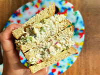 Hand holding a sandwich made with Fishwife Albacore Tuna with Spanish Lemon over a colorful plate on a wood table