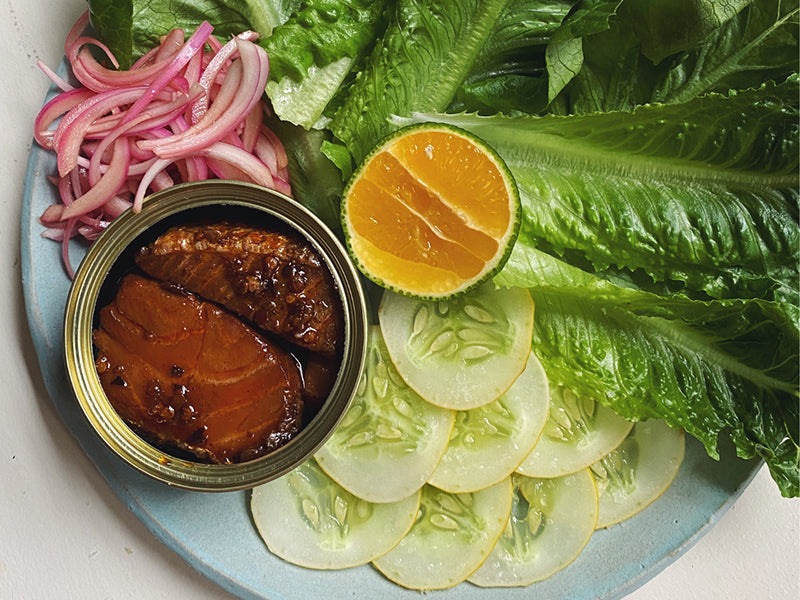 Fishwife Smoked Salmon with Fly By Jing Chili Crisp in Open Tin on Plate with Lettuce, Onion, and Cucumber
