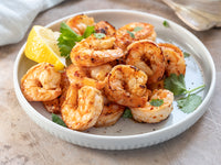 White plate with grilled shrimp, lemon, and parsley on a wooden surface