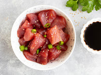 Ahi Tuna cubes with sesame and green onions on a marble surface with soy sauce and herbs