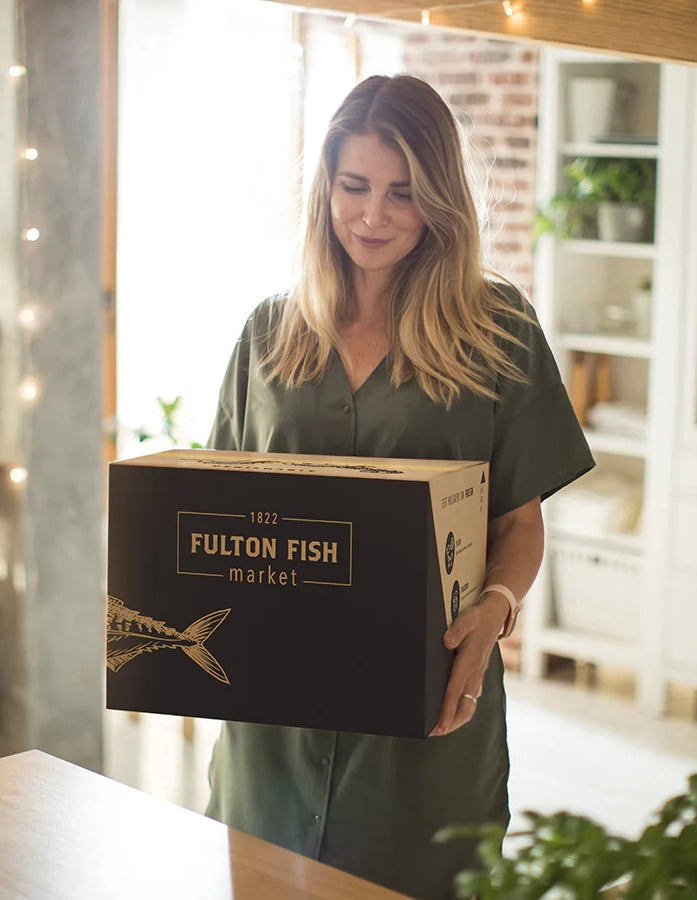 Woman Holding a Fulton fish Market Box Walking Into the Kitchen to Open and Unpack Her Seafood