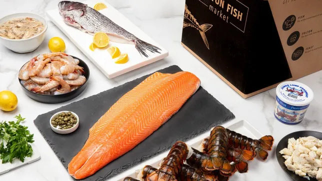 Fulton Fish Market Box on Marble Surface with Shrimp, Crabmeat, Lobster Tails and Salmon fillet on Plates