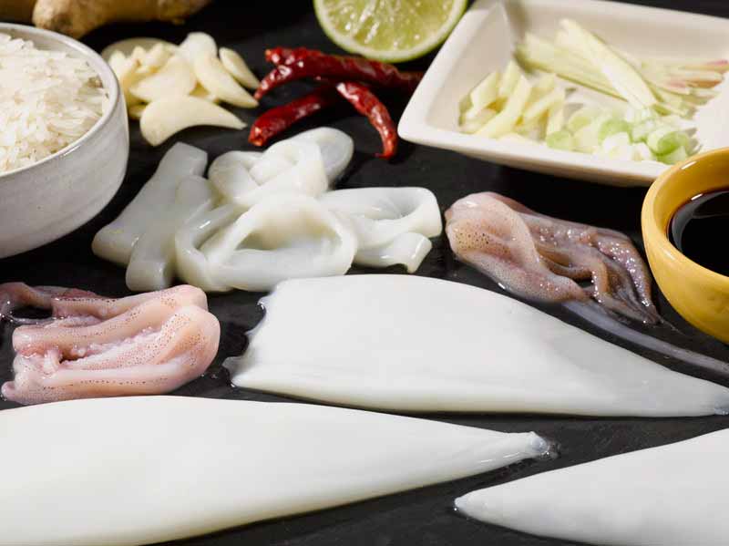 Fresh Squid Tubes and Tentacles on Dark Surface with Herbs and Spices