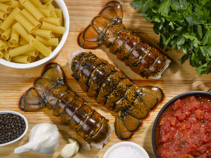 Large Cold Water Lobster Tails on Cutting Board with Herbs, Spices, Tomatoes and Pasta